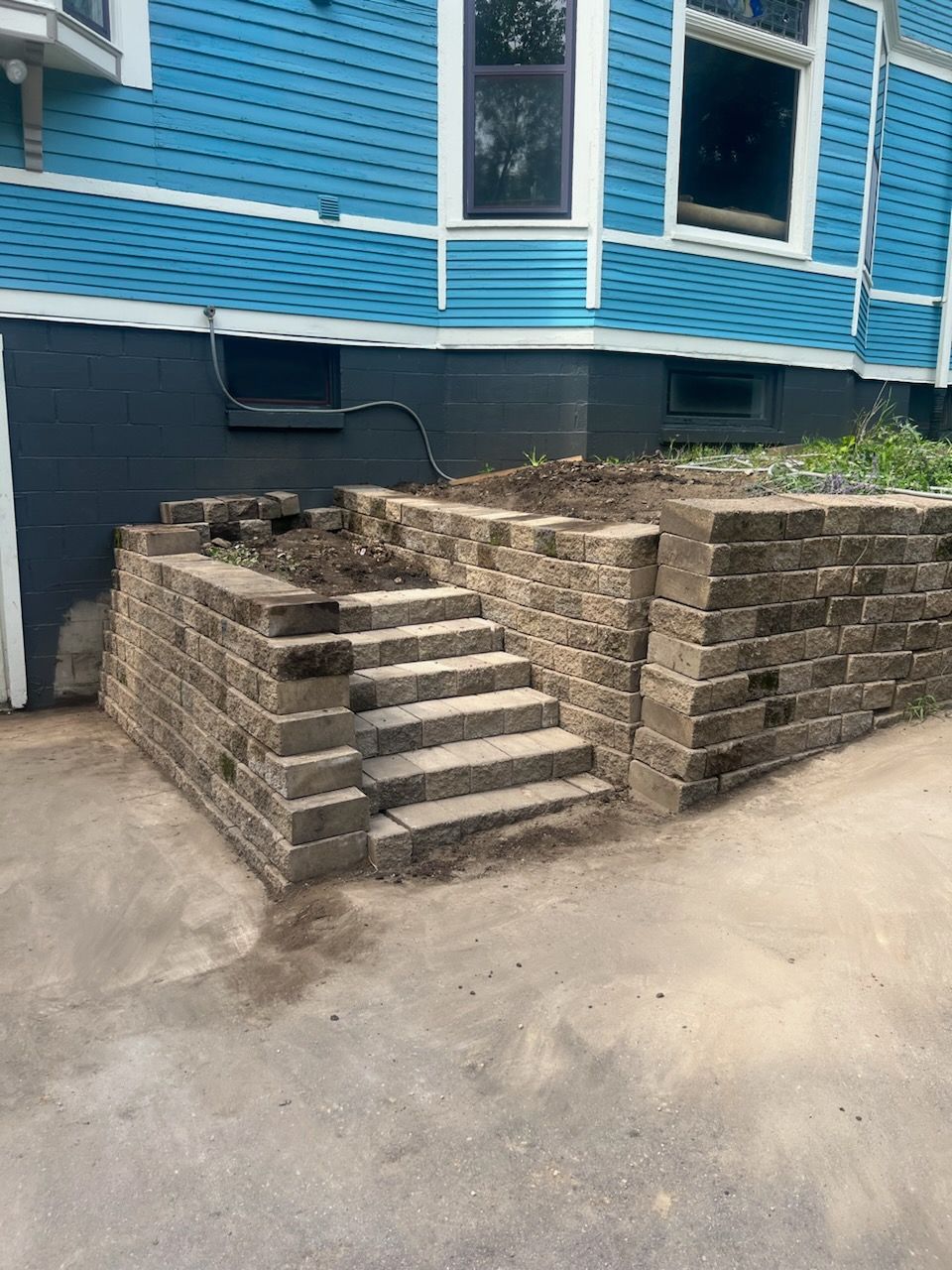 A blue house with a brick wall and stairs in front of it.