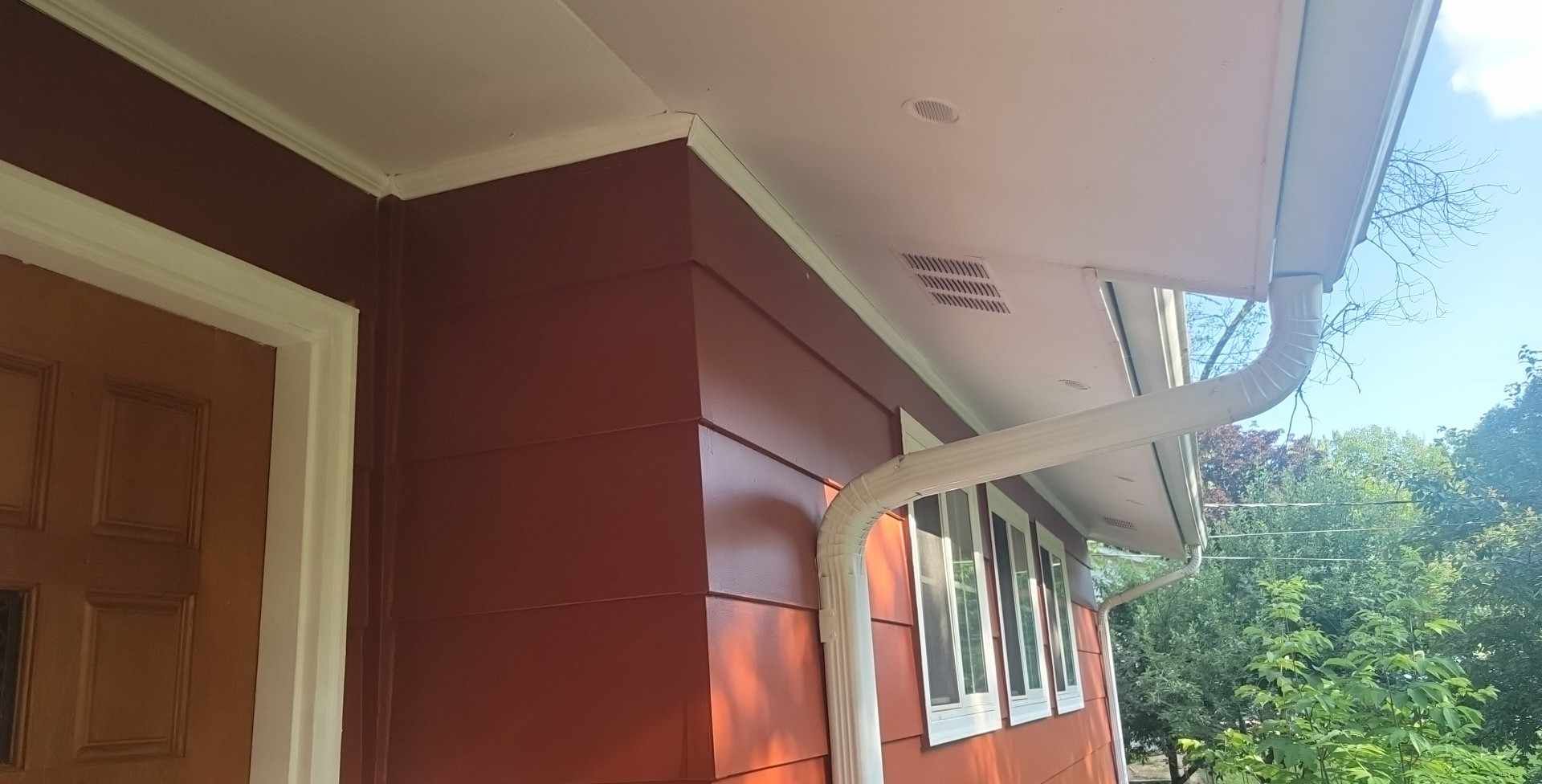 A red house with a white gutter on the side of it.