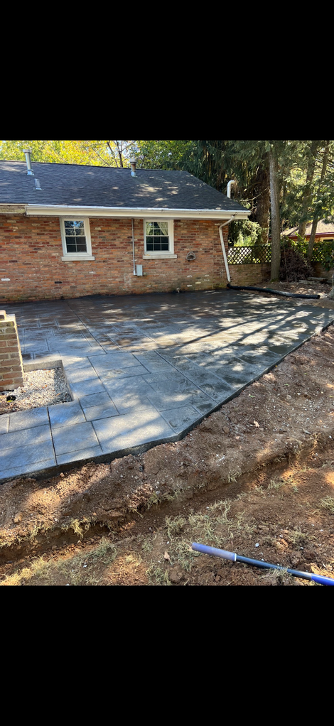 Brick building with concrete patio, surrounded by dirt and trees, sunny day.