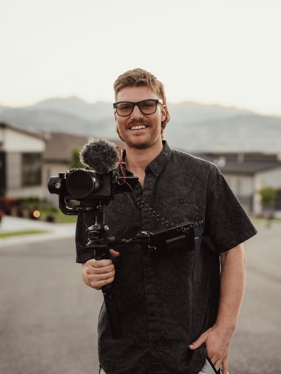 Trace Bodin is holding a camera and smiling while standing on a street.