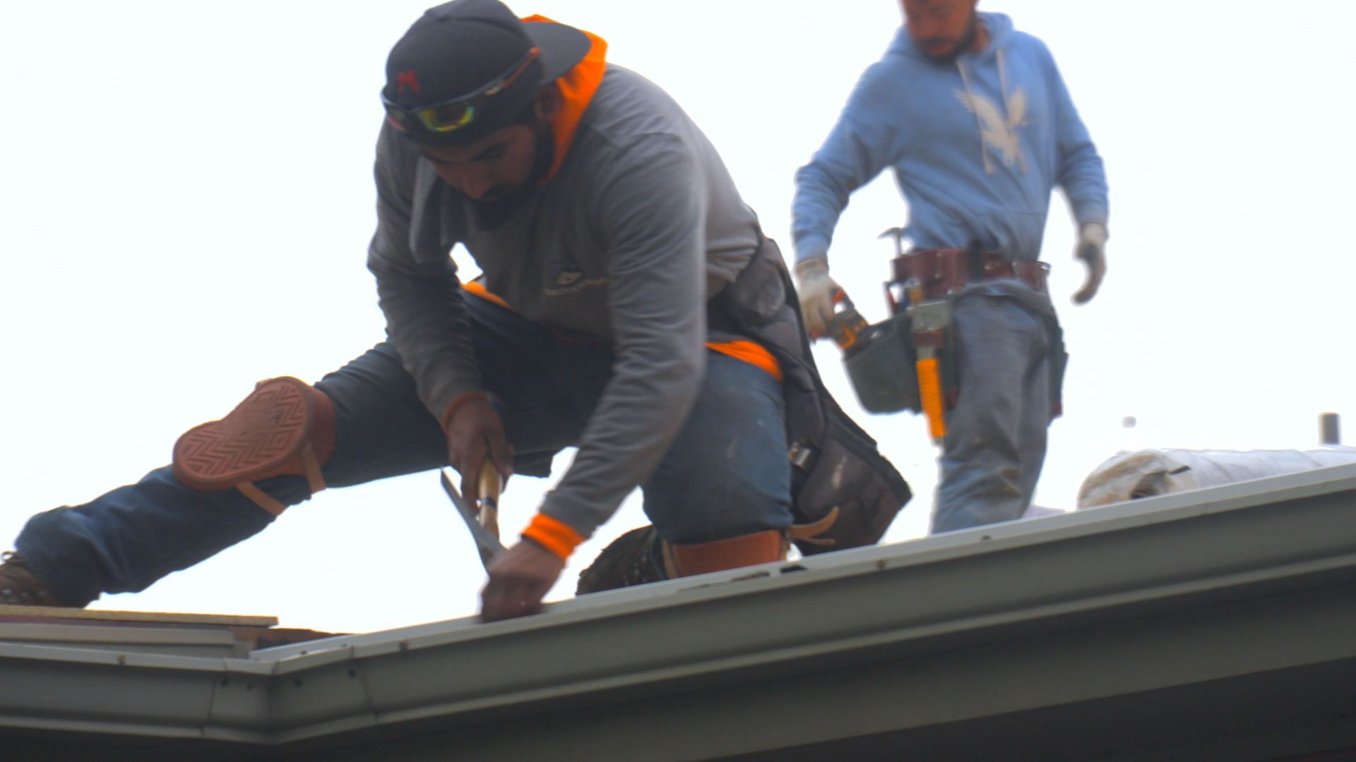 Roofers replacing shingles on a residential rooftop under clear skies.