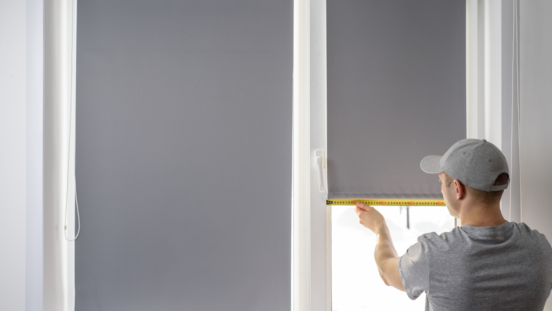 A man is measuring a window blind with a tape measure.