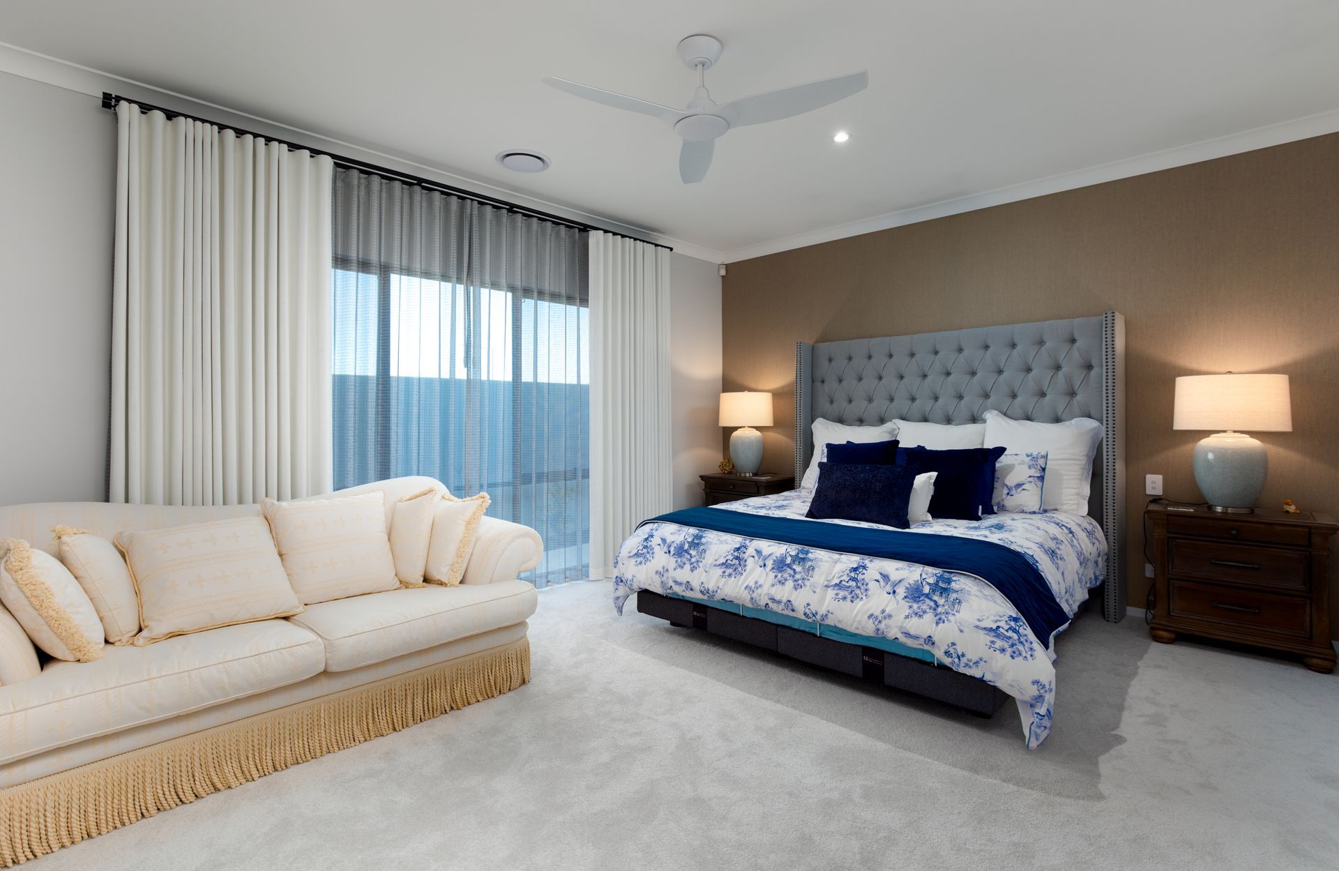 A bedroom with a bed , couch , nightstands and a ceiling fan.