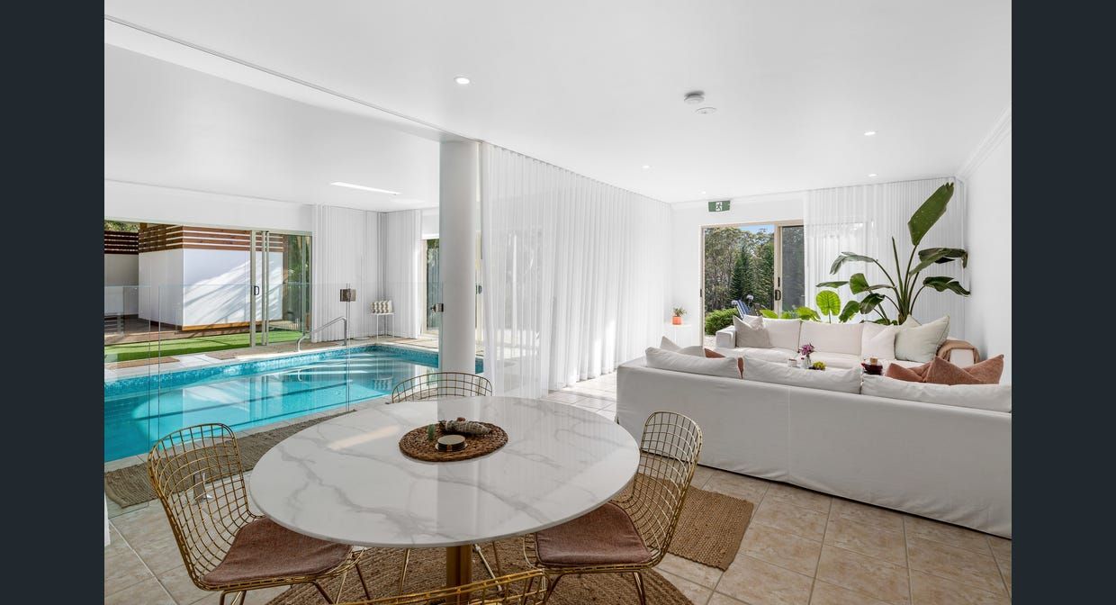A living room with a table and chairs and a swimming pool in the background.