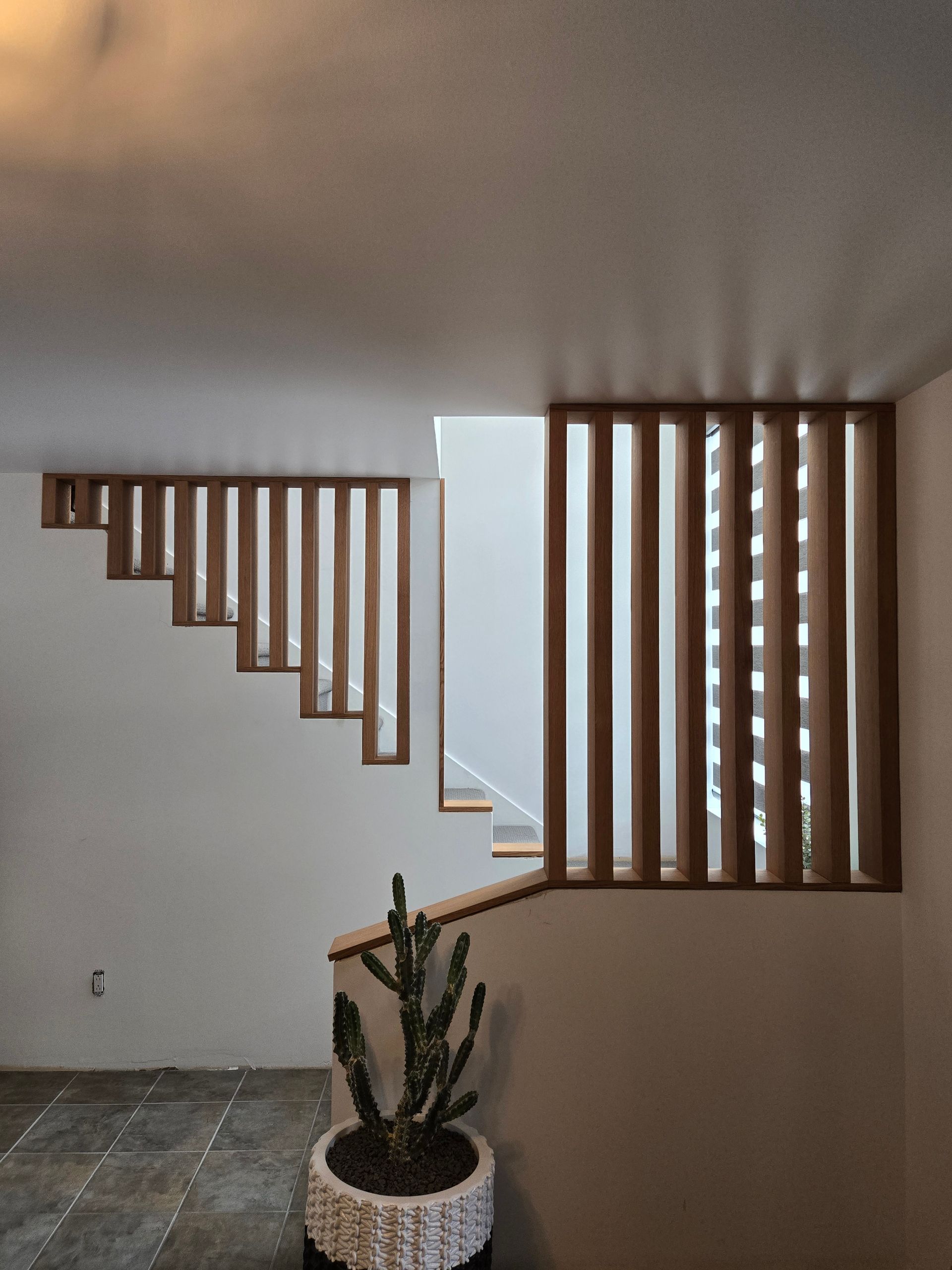 Escalier en bois avec rampe &agrave; lattes dans un int&eacute;rieur moderne, plante succulente en pot au premier plan.