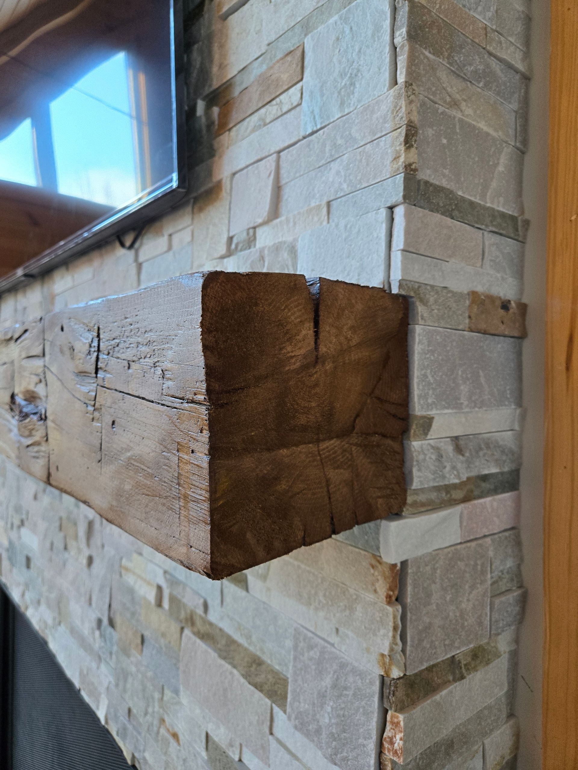 Un manteau en bois est posé sur une cheminée en pierre.