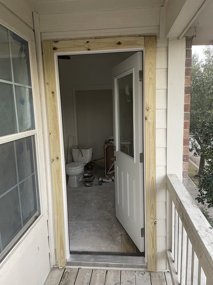 A view from a wooden porch looking through an open door into a room under renovation with a toilet visible inside.