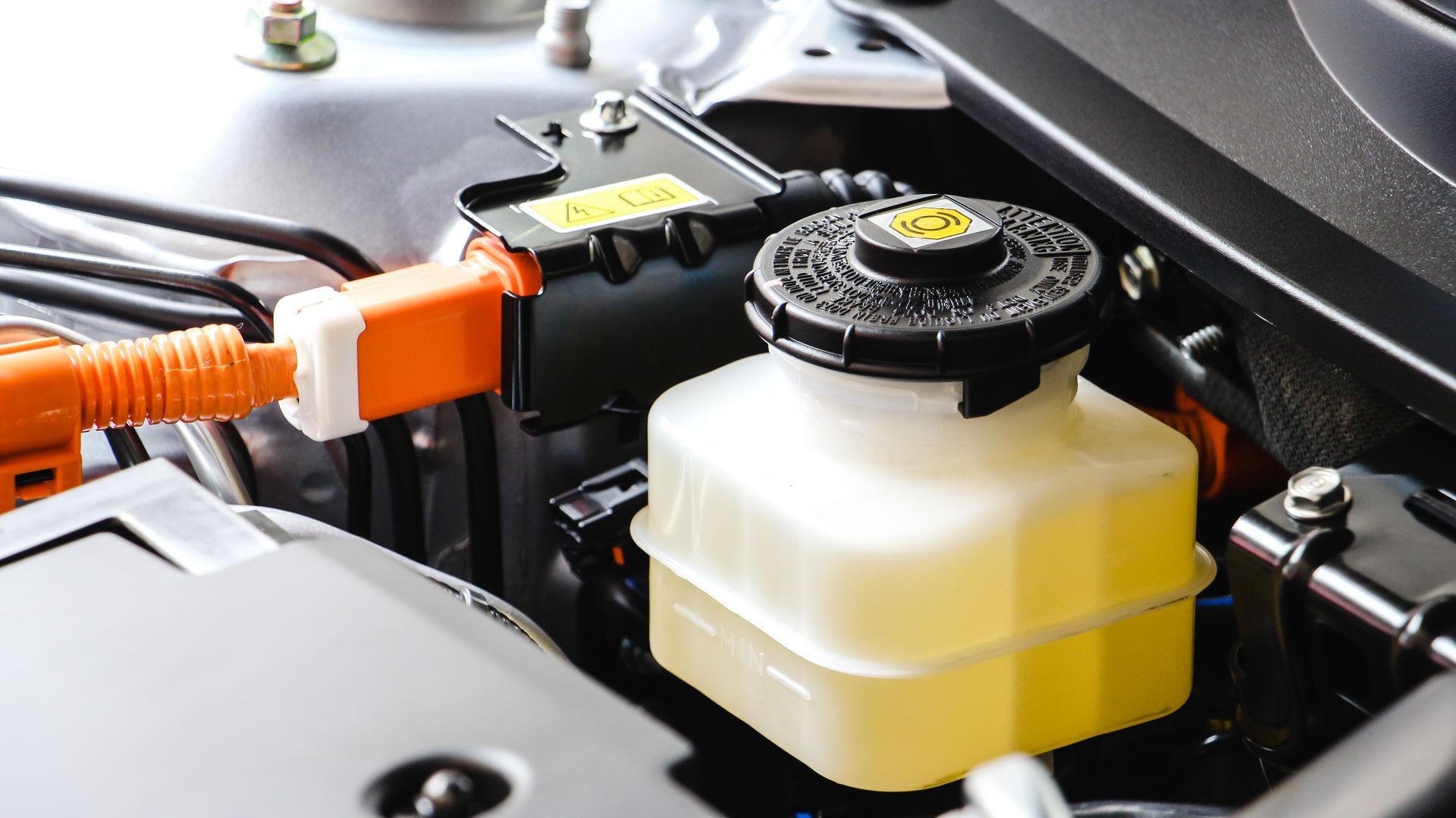 Close-up of an orange EV charging connector plugged into a car’s engine compartment beside a fluid reservoir