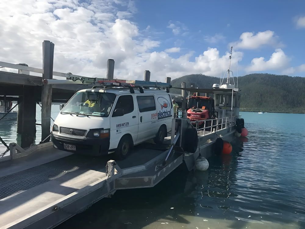 A White Van Is Parked On A Dock Next To A Body Of Water — Reef Electrical in Cannonvale, QLD
