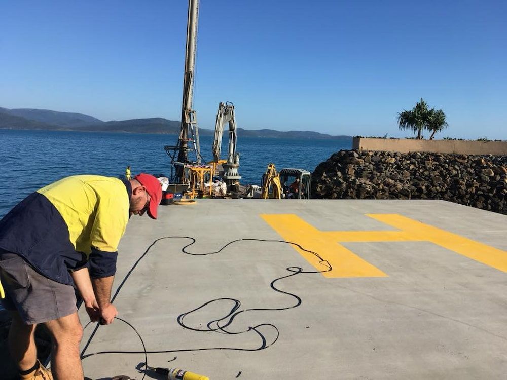 A Man Is Working On A Concrete Surface Near The Water — Reef Electrical in Cannonvale, QLD