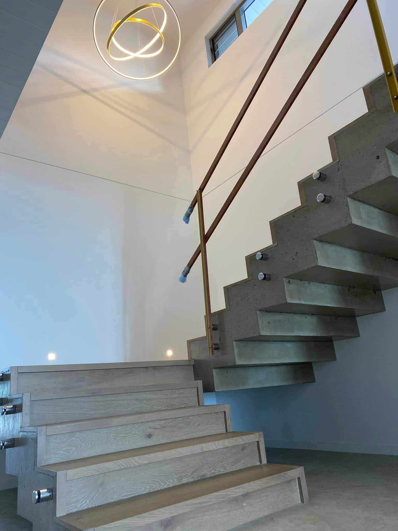 a Staircase With a Wooden Railing and a Light Hanging From the Ceiling — Reef Electrical in Cannonvale, QLD