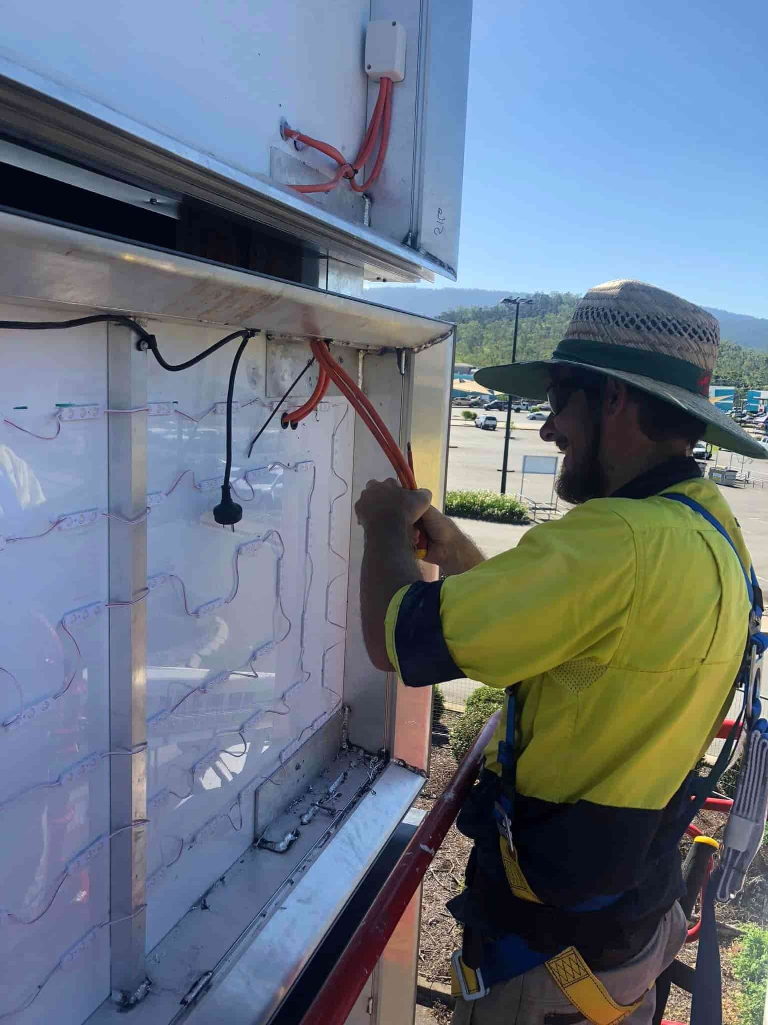 a Man in a Yellow Shirt and Hat is Working on a Sign — Reef Electrical in Bowen, QLD