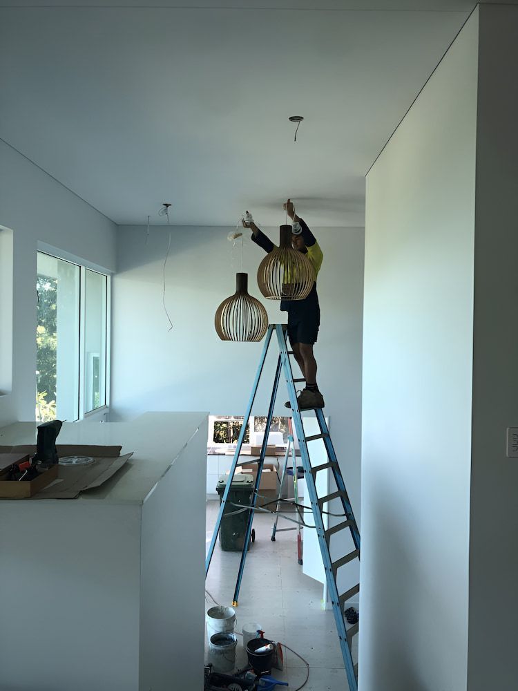 A Person Is Standing On A Ladder In A Room Holding A Light Bulb — Reef Electrical in Cannonvale, QLD