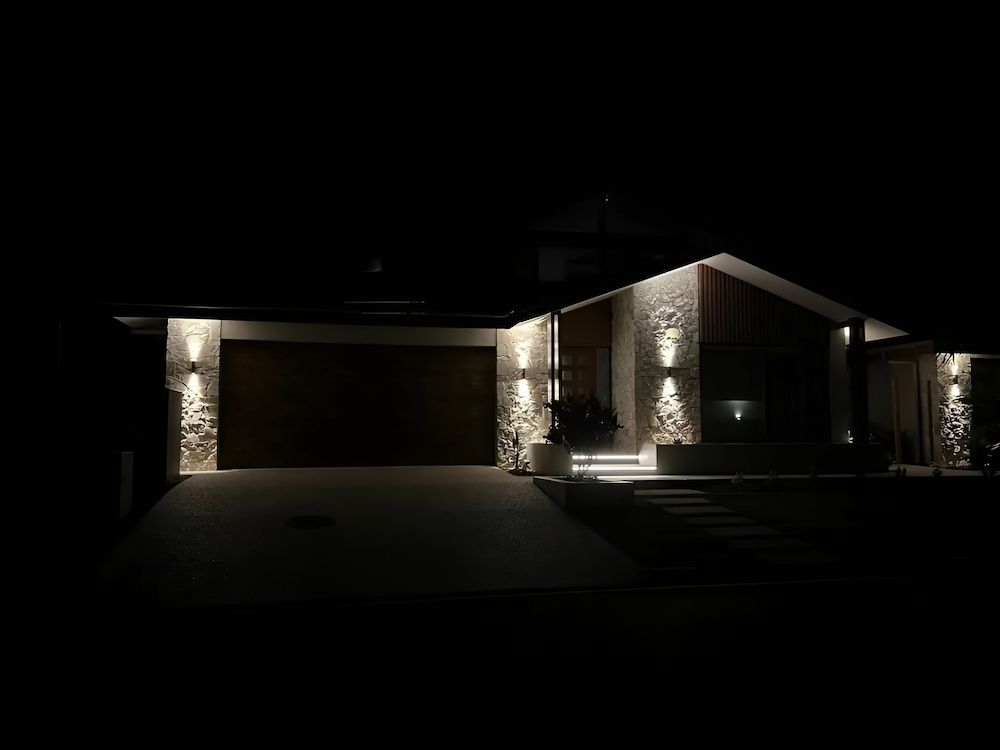 A House Is Lit Up At Night With A Garage Door Open — Reef Electrical in Cannonvale, QLD
