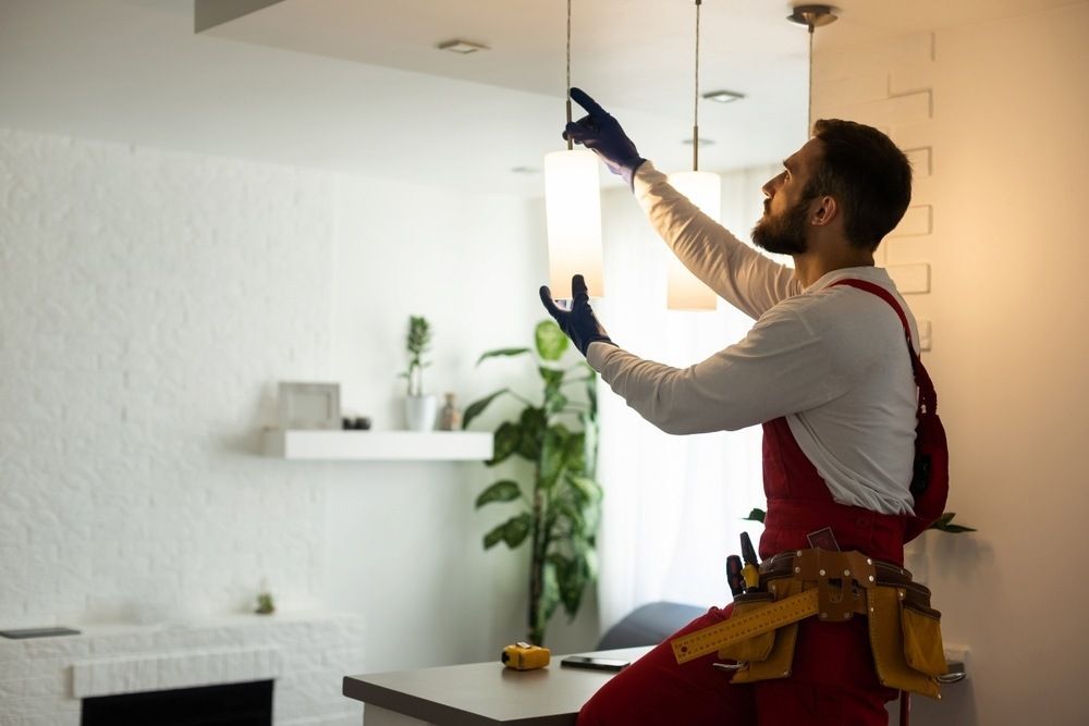 A Man Is Fixing A Light Fixture In A Living Room — Reef Electrical in Airlie Beach, QLD