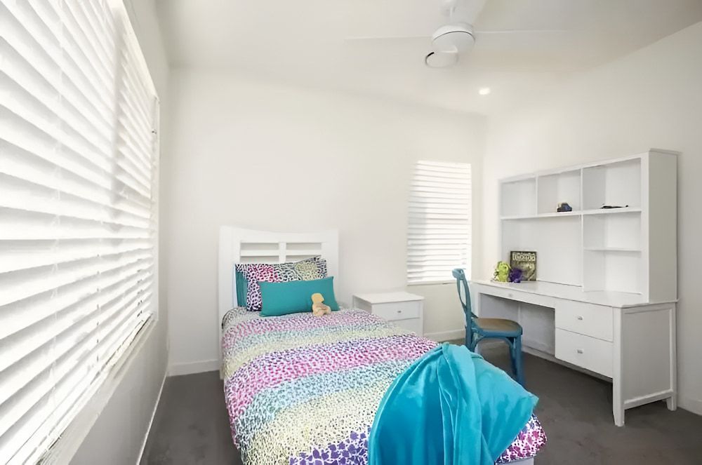 A Bedroom With A Bed, Desk, And Window — Reef Electrical in Cannonvale, QLD