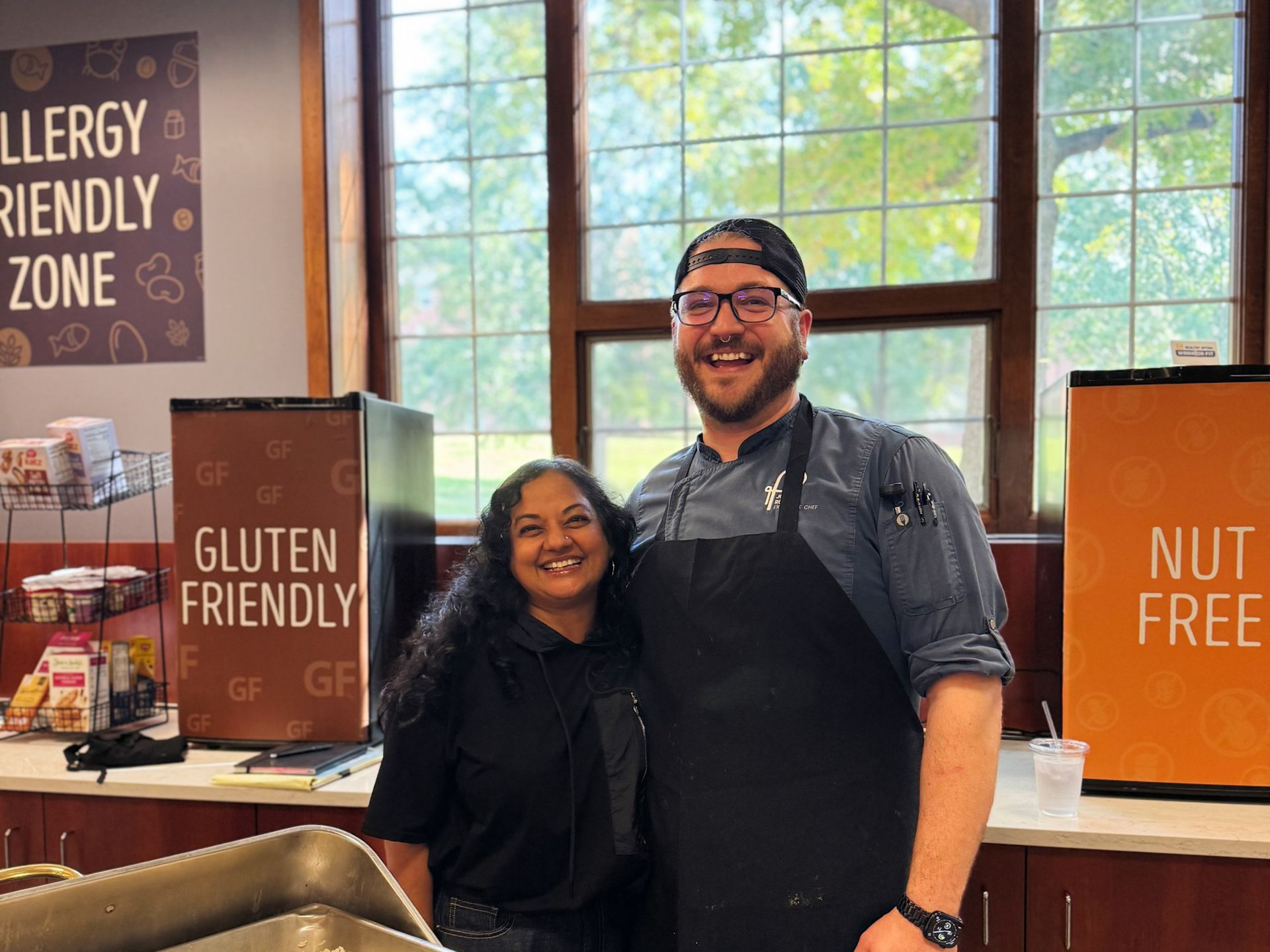 Two people smiling next to food serving station, with