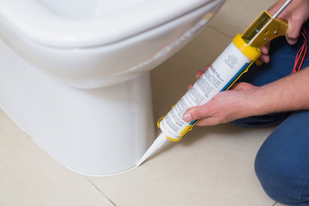 A Person Is Applying Silicone To A Toilet — Jobs2BDone in Woy Woy, NSW