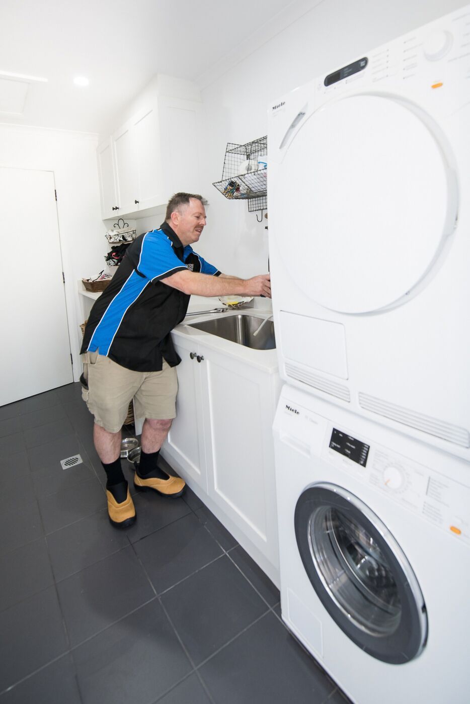 A Man Is Working On A Washer And Dryer In A Laundry Room  — Jobs2BDone in Woy Woy, NSW