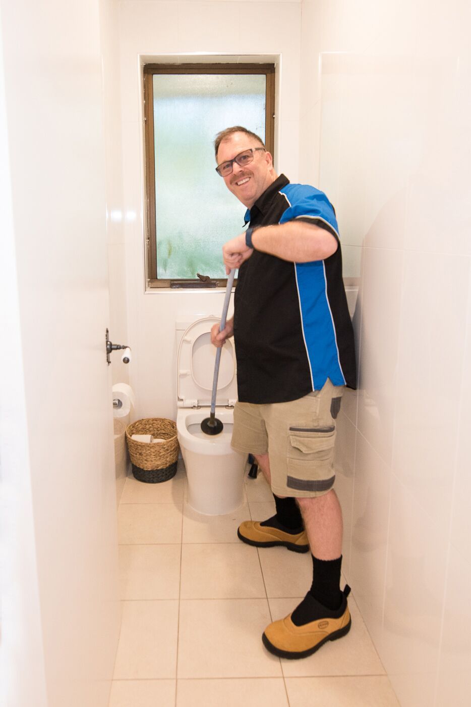 A Man Is Standing Next To A Toilet In A Bathroom Holding A Plunger  — Jobs2BDone in Woy Woy, NSW