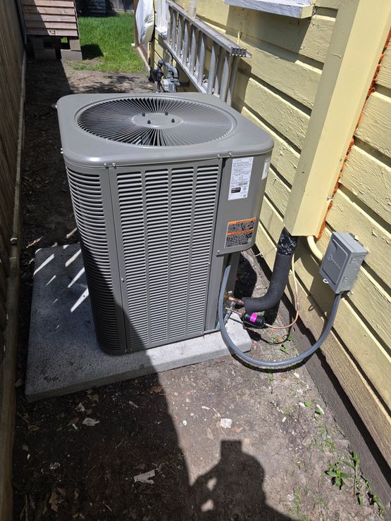 Two gray outdoor air conditioning units beside a brick house wall