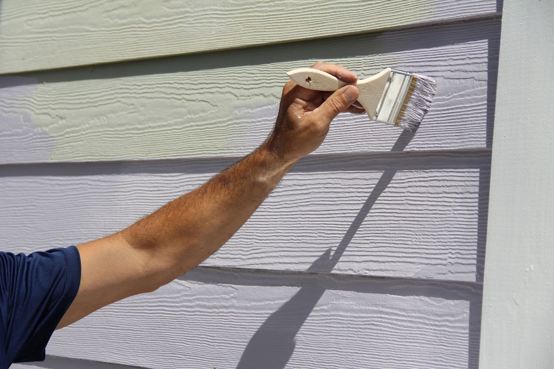 Close-up of a man's hand painting the exterior of a house.