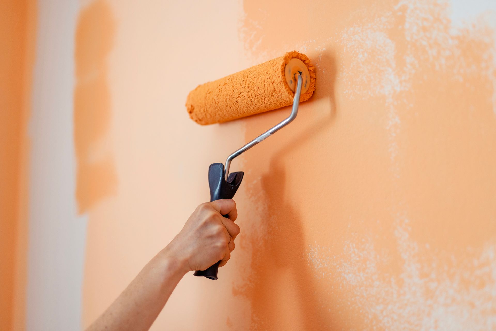 Hand using orange paint roller on orange wall.