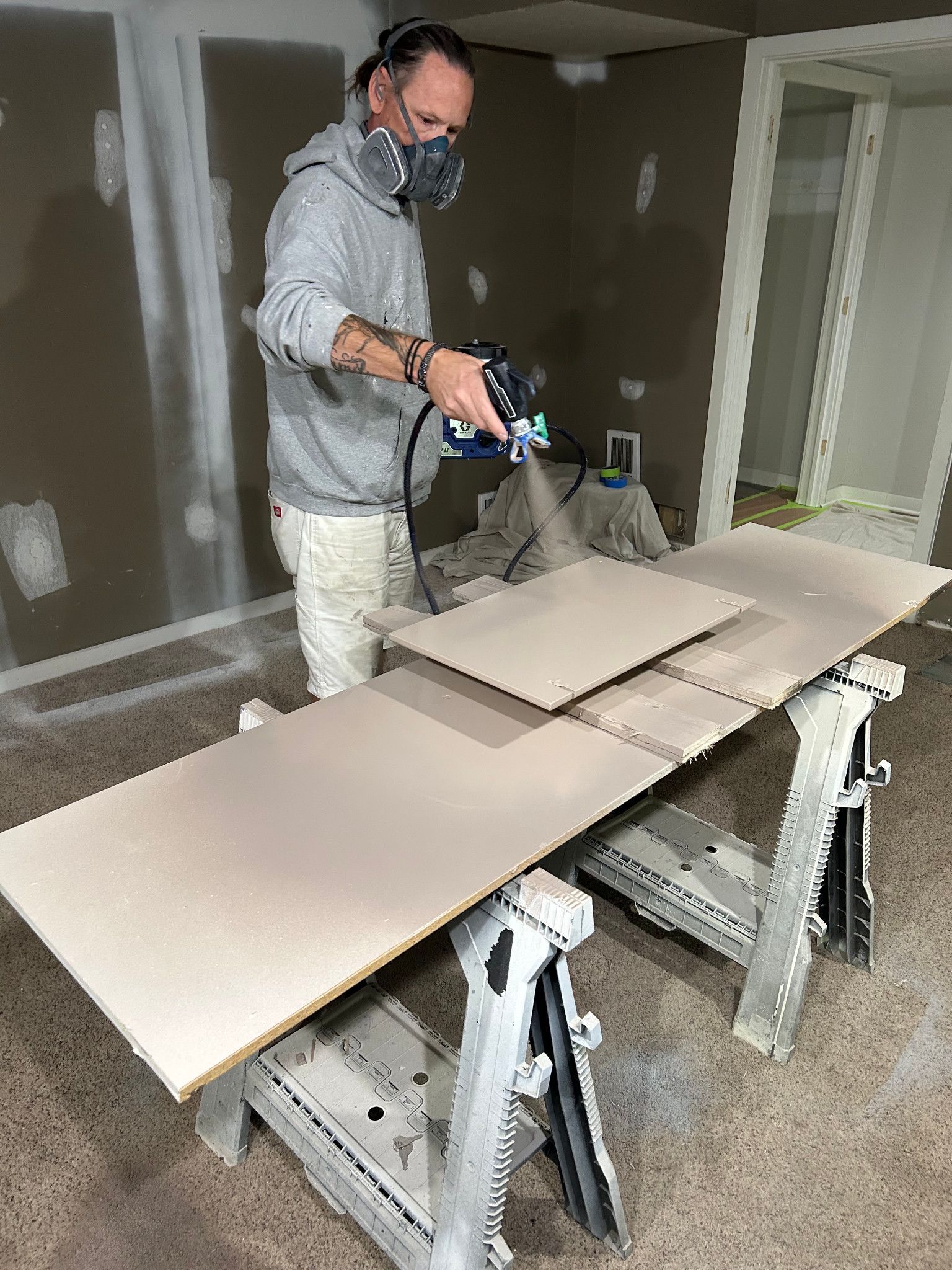 Painter wearing a respirator spray-painting cabinet doors on sawhorses.