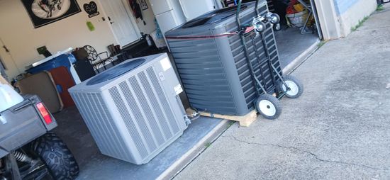 Several outdoor air conditioning units on a driveway beside a garage.