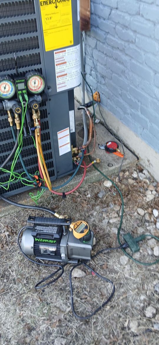 Outdoor HVAC service setup with gauges, hoses, and a vacuum pump beside a wall-mounted unit