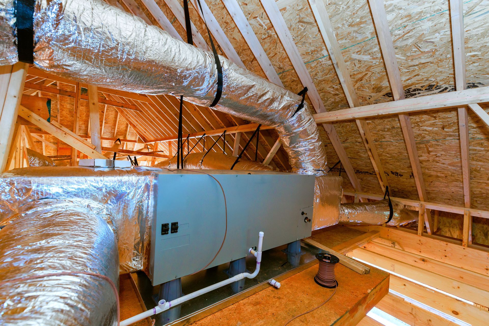 Attic HVAC unit with silver ductwork and exposed wooden roof rafters