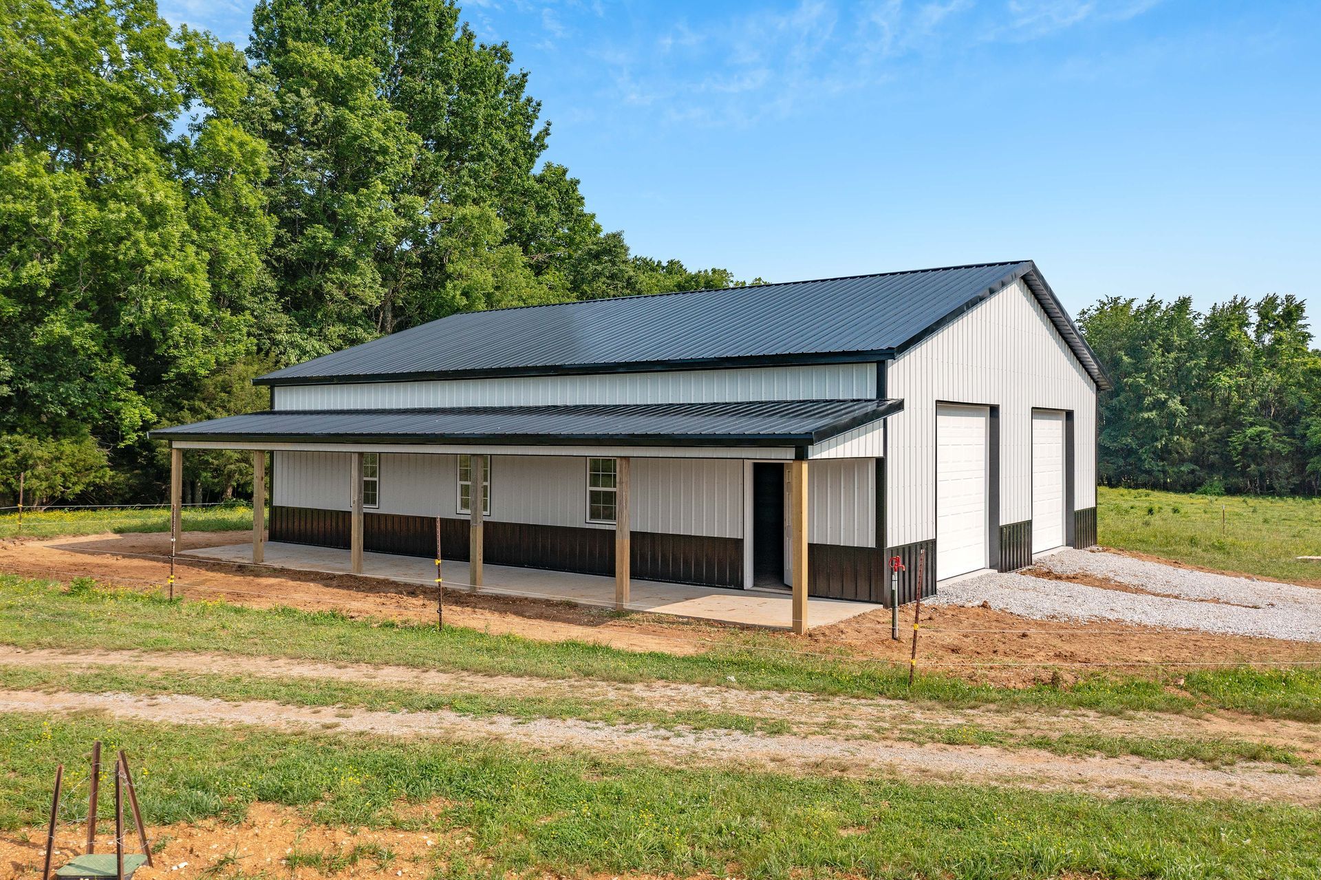 A large white barn with a black roof is sitting in the middle of a grassy field.