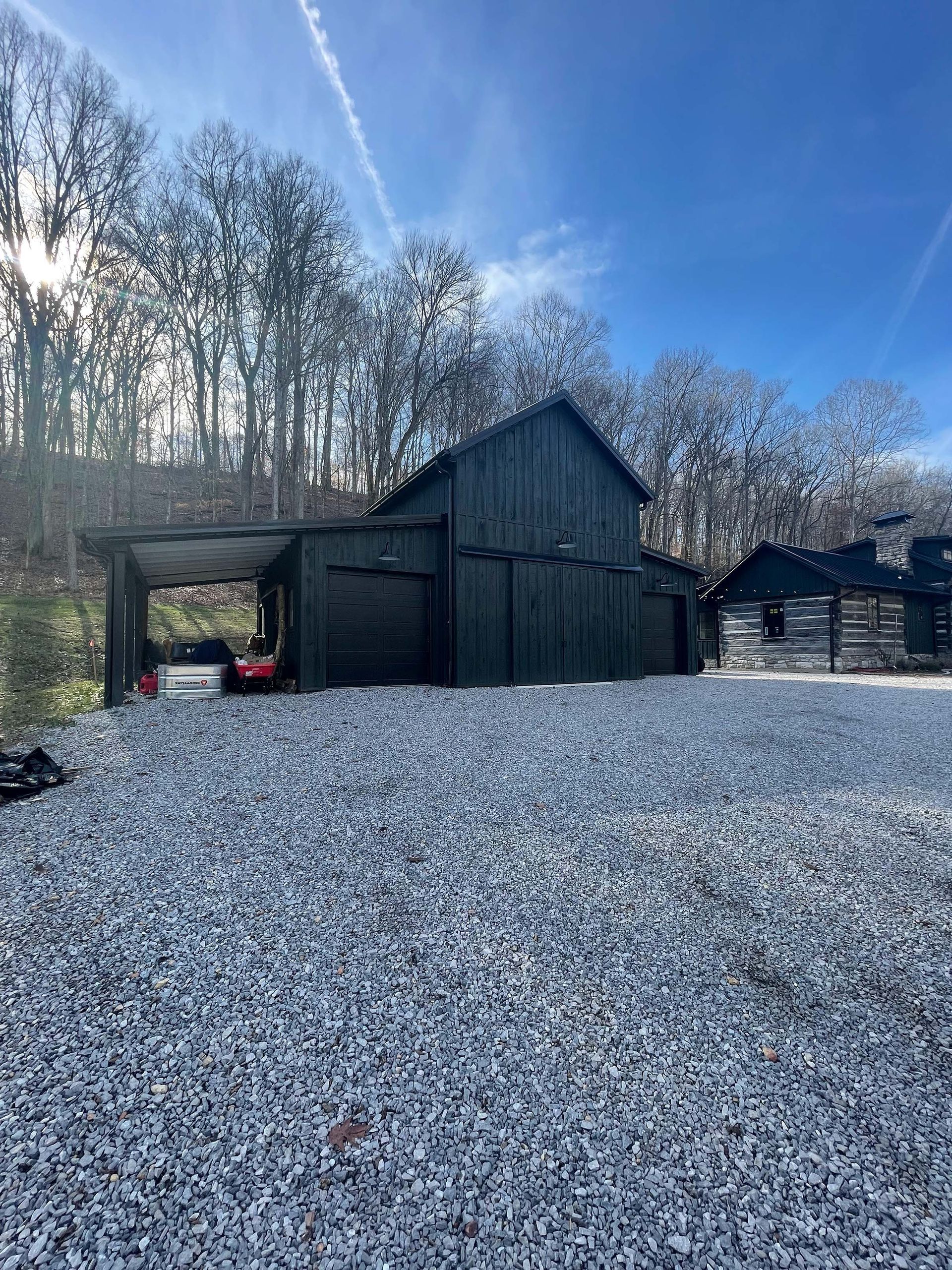 A black barn is sitting in the middle of a gravel driveway.