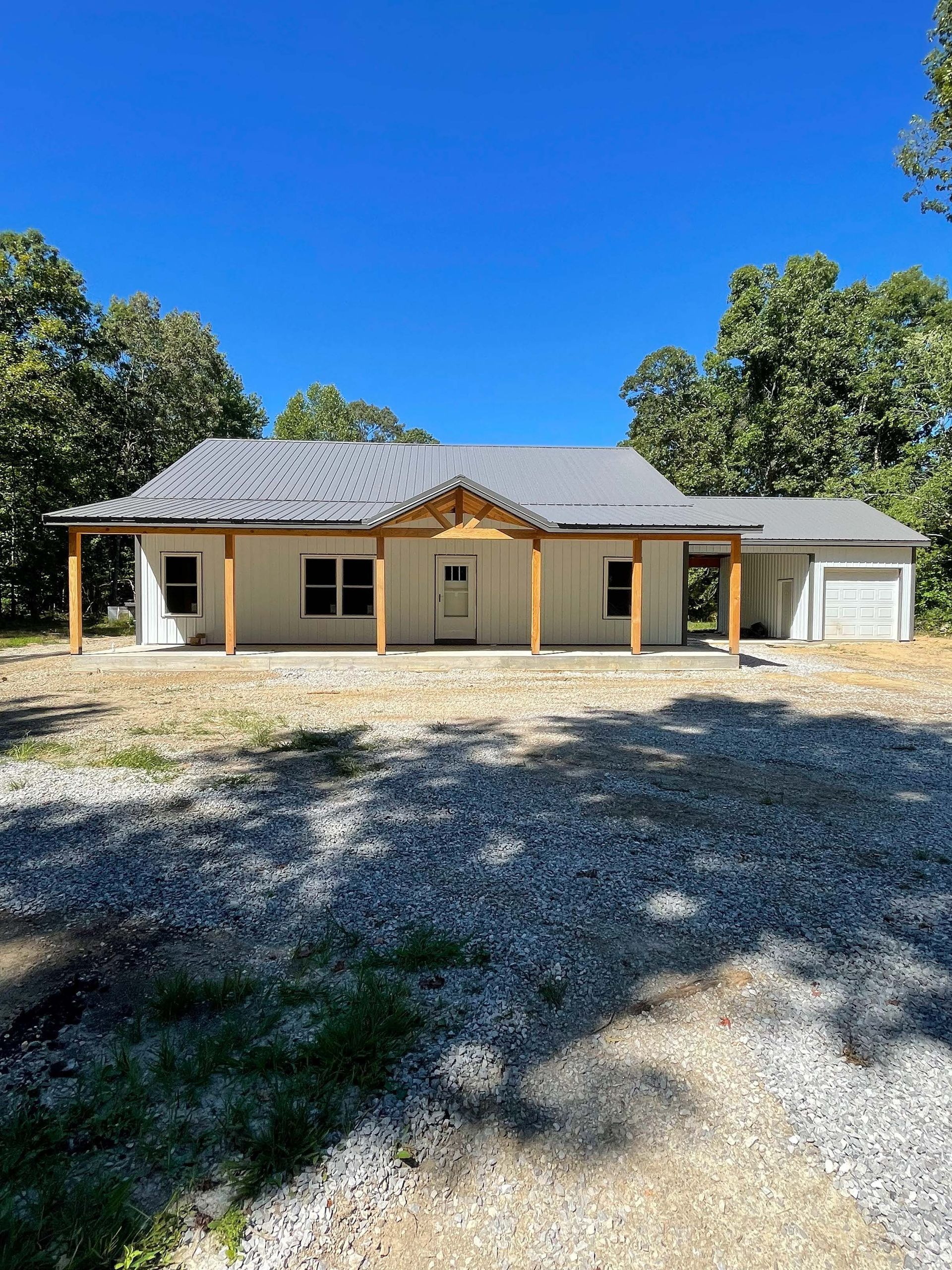 A white house with a porch and a garage is sitting on top of a gravel lot.
