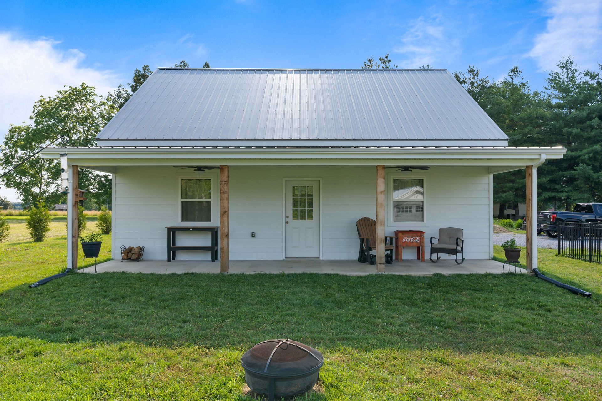 A small white house with a metal roof is sitting in the middle of a grassy field.