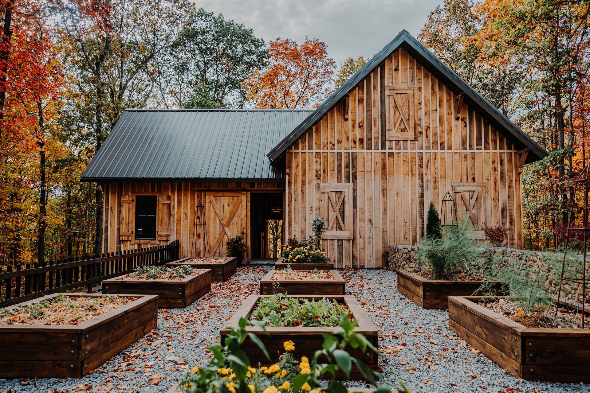 A wooden barn with a black roof and a garden in front of it.