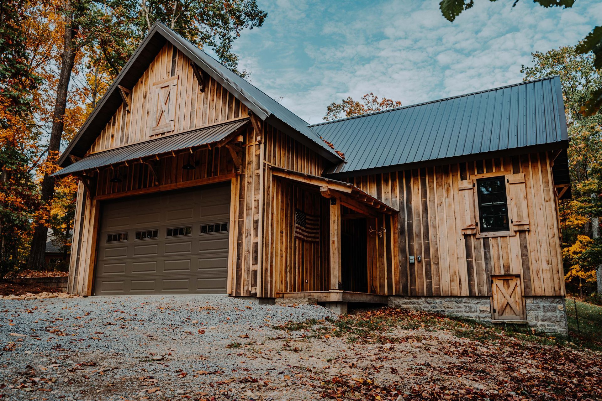 A wooden house with a garage and a black roof is surrounded by trees.