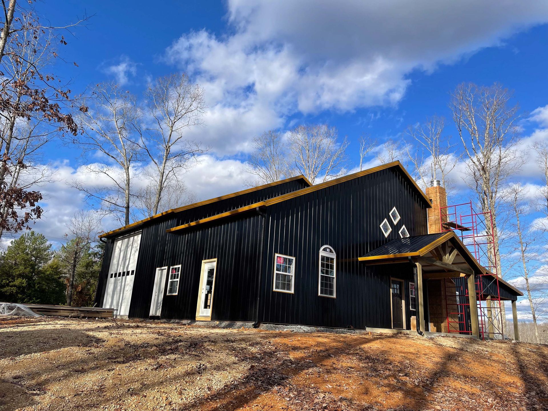 A large black barn is sitting on top of a dirt field.
