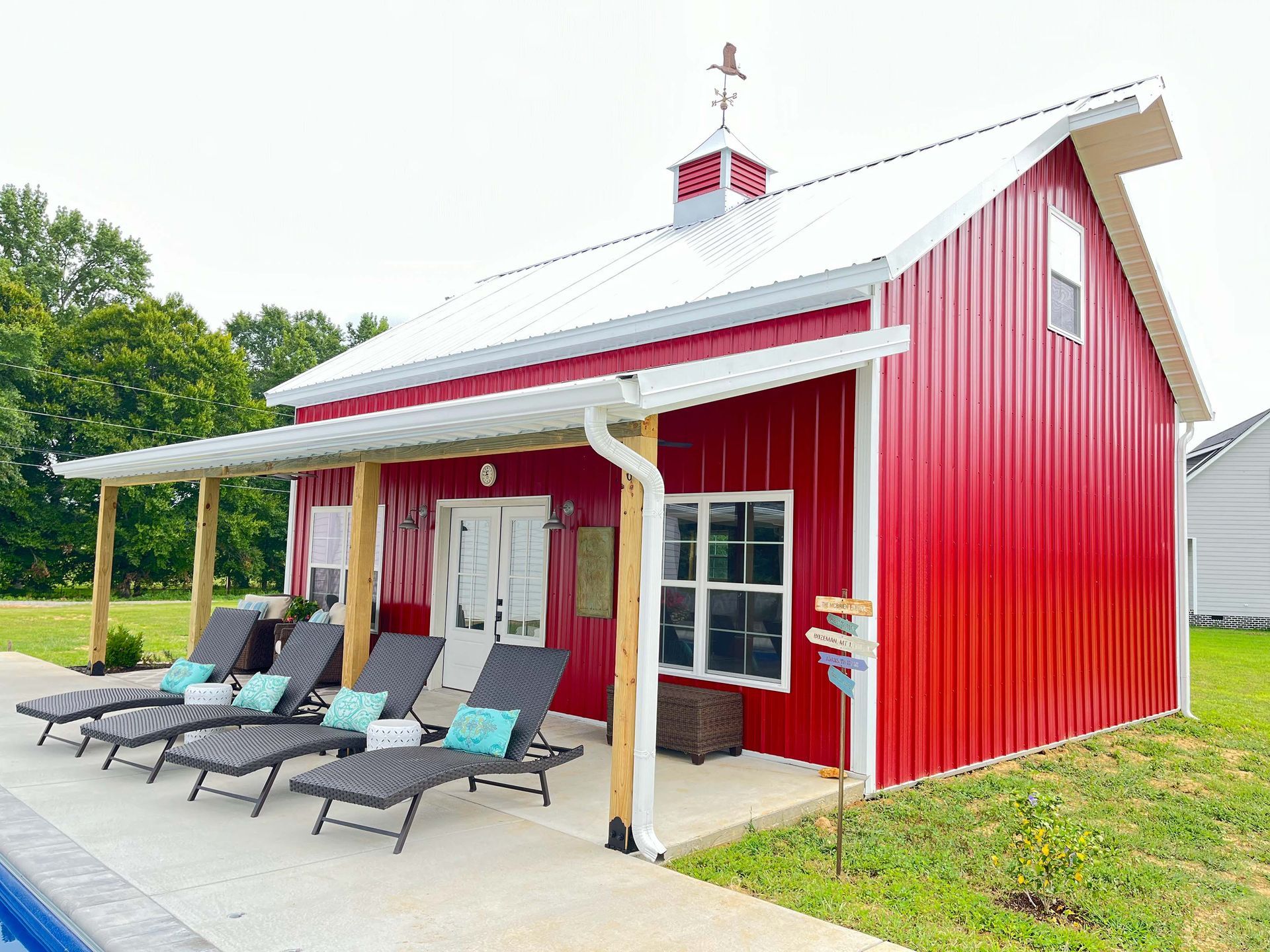 A red barn with a white roof is next to a swimming pool.