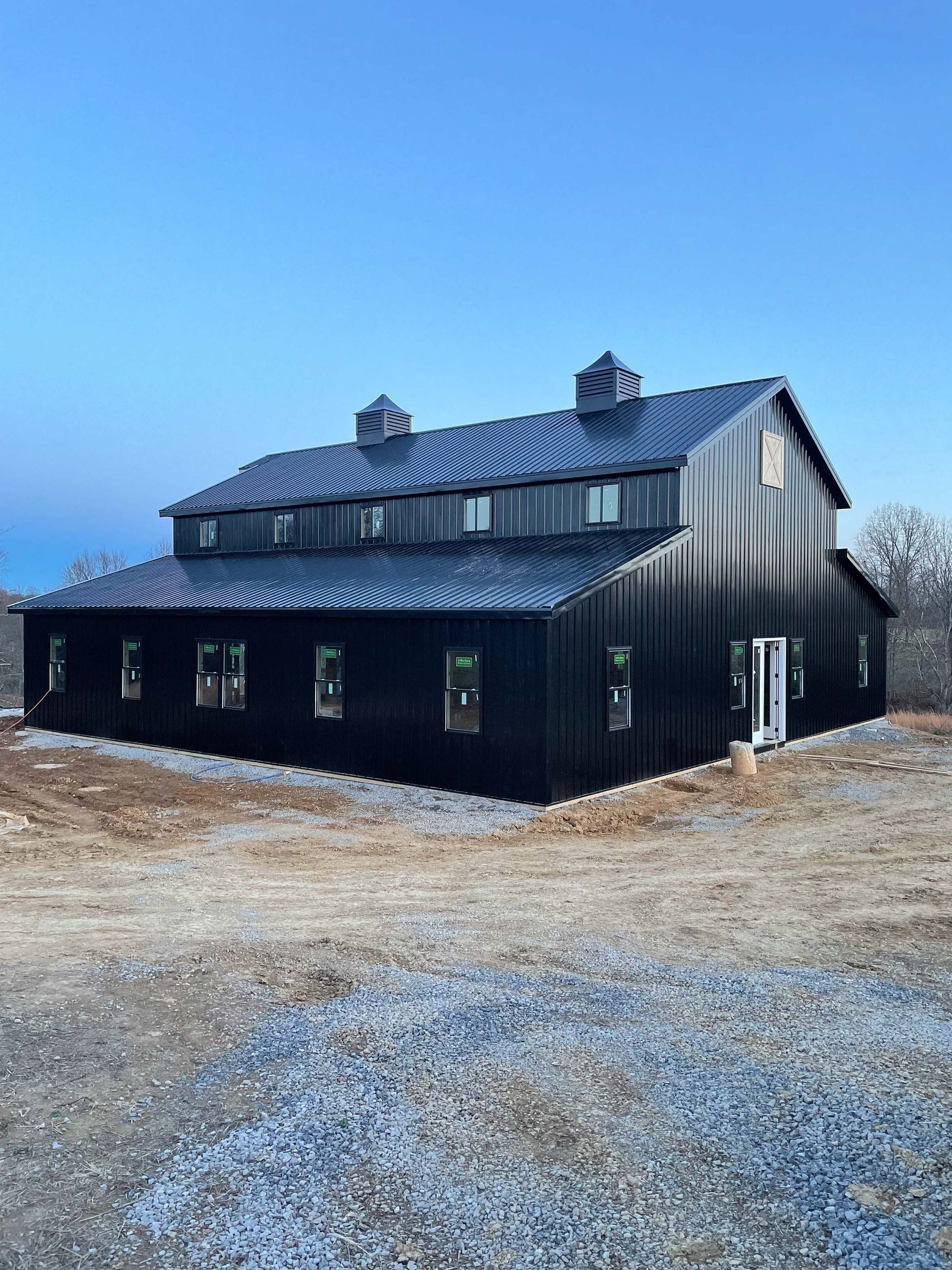 A large black barn is sitting in the middle of a dirt field.