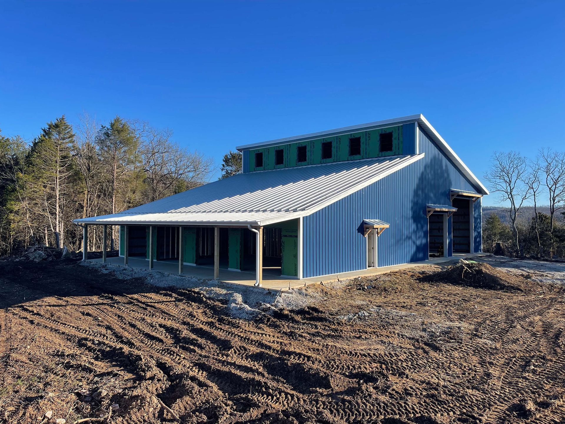 A blue barn with a porch is sitting in the middle of a dirt field.
