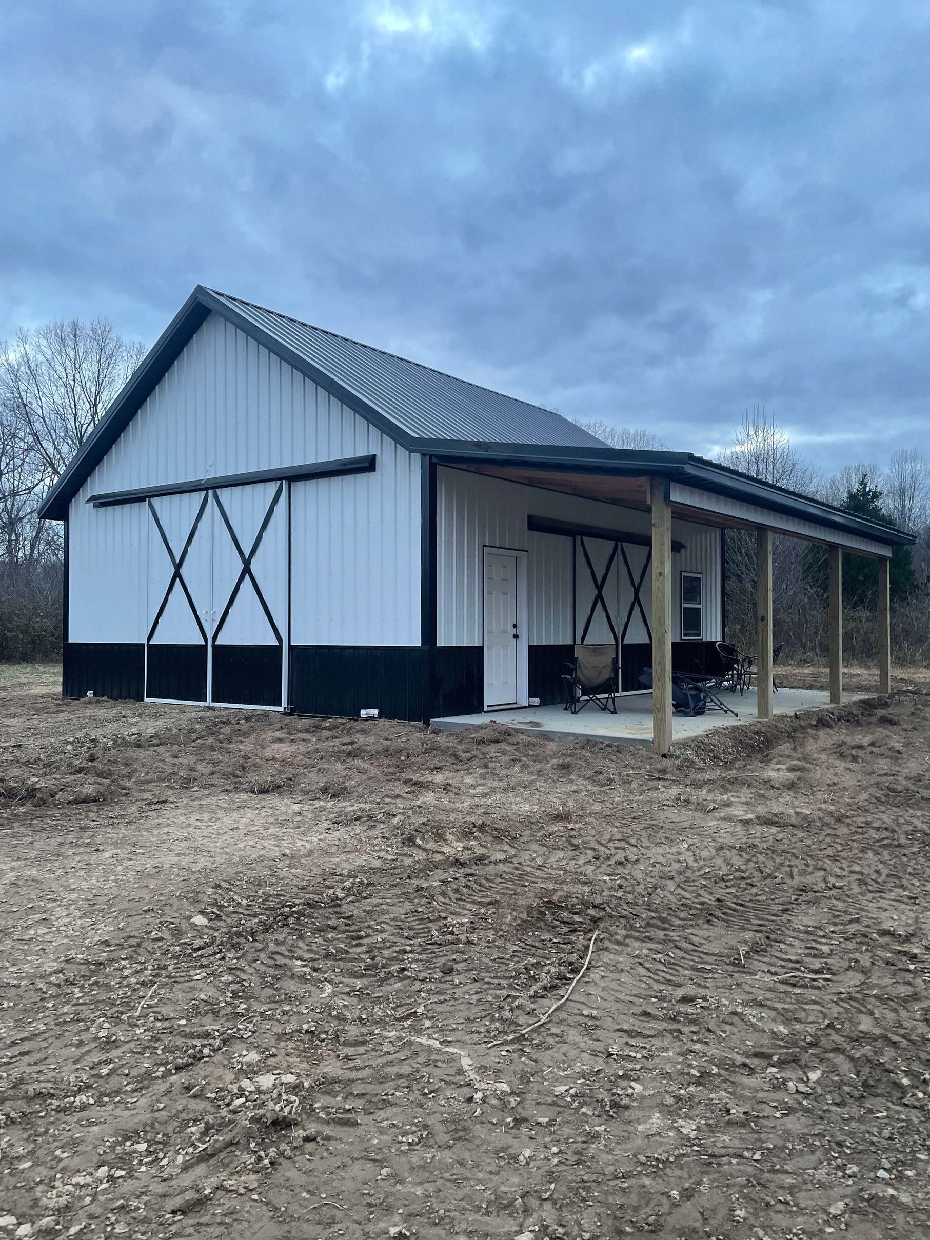 A white and black barn with a porch in a field.