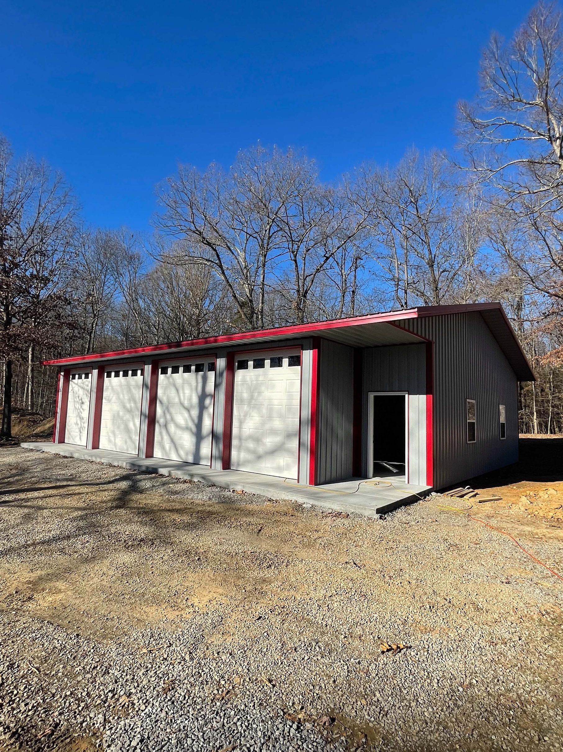 A white garage with a red roof is sitting in the middle of a dirt field.