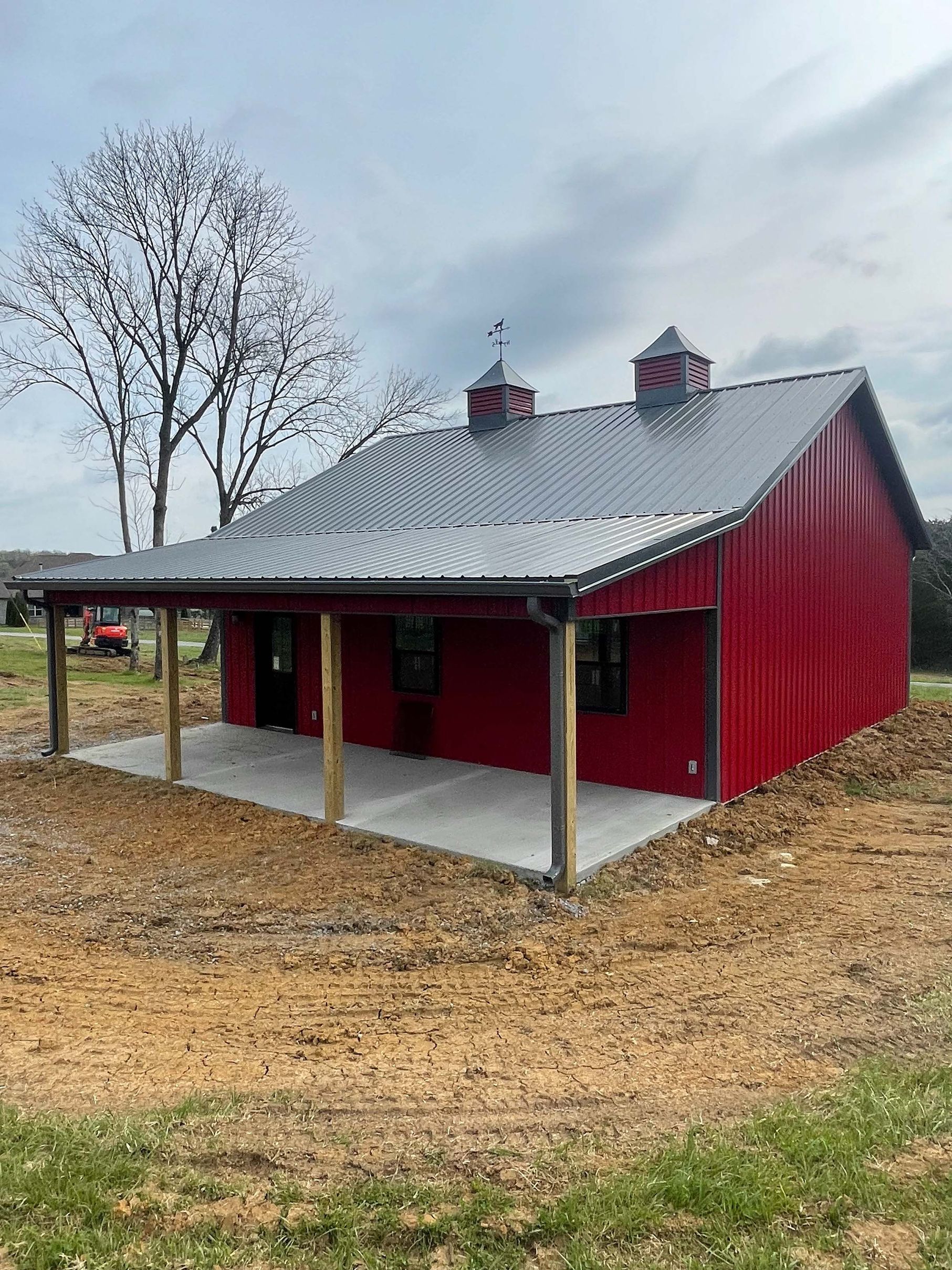 A red barn with a metal roof and a porch in a field.