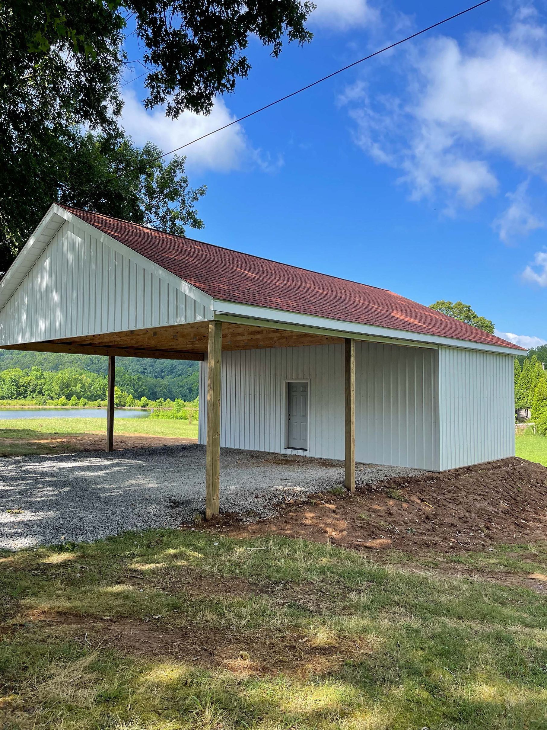 A white barn with a red roof is sitting in the middle of a grassy field.