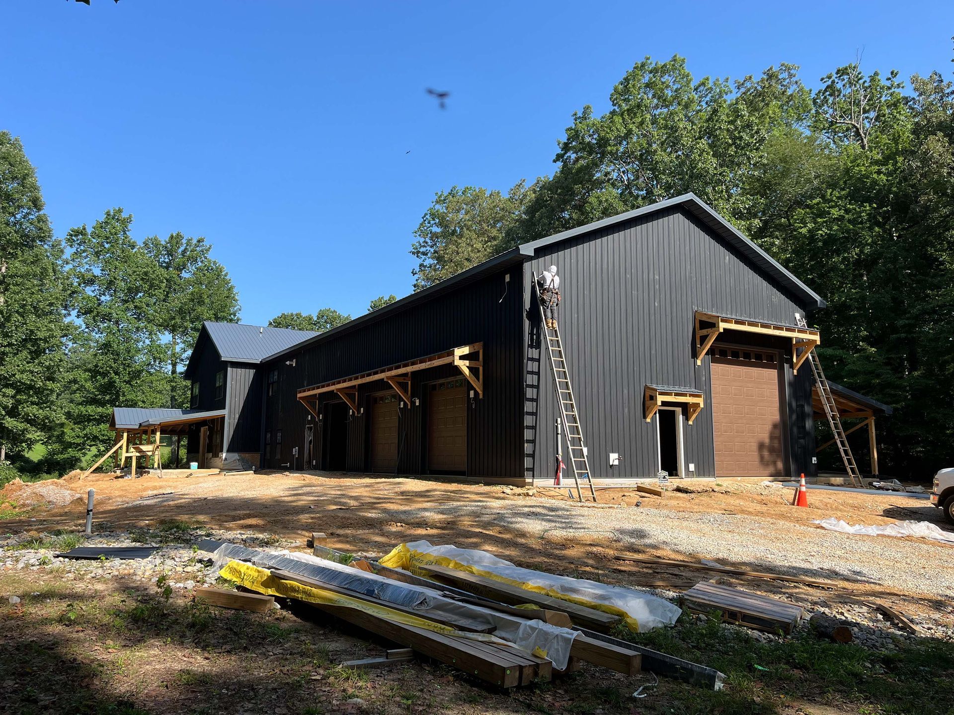 A large black barn is being built in the middle of a forest.