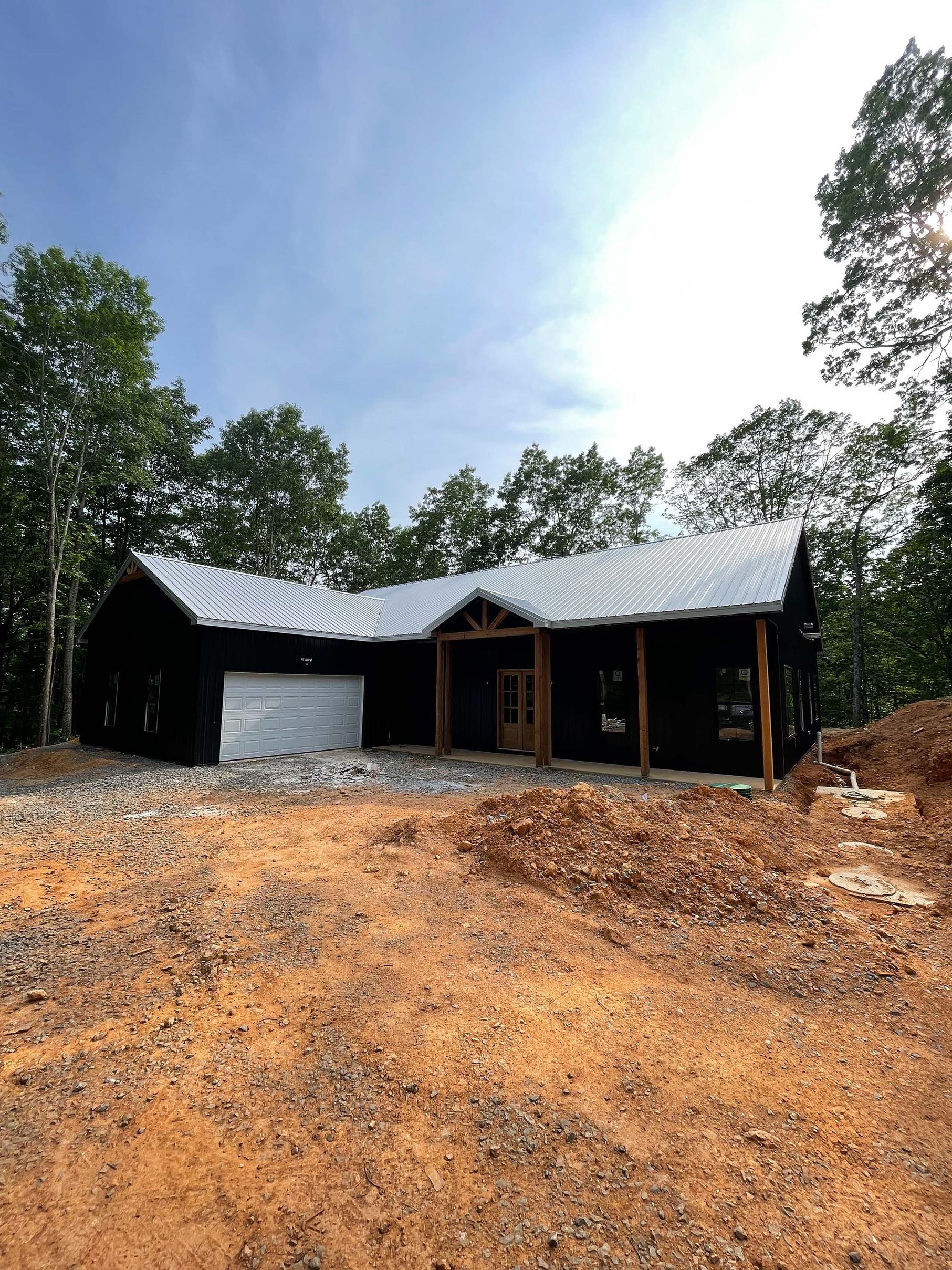 A black house with a metal roof is sitting in the middle of a dirt field.