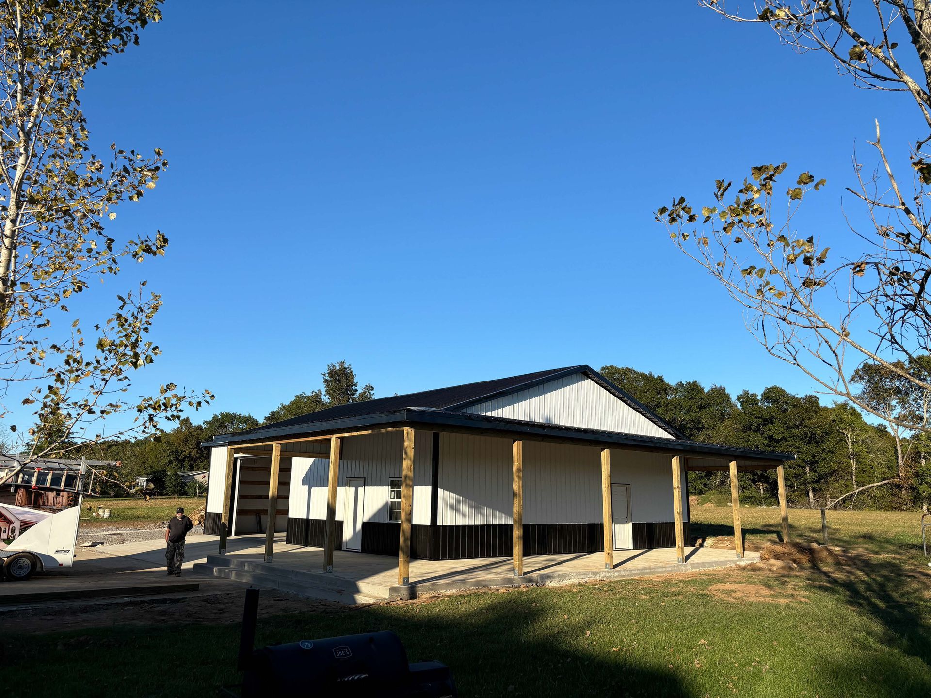 A white building with a black roof is sitting in the middle of a grassy field.