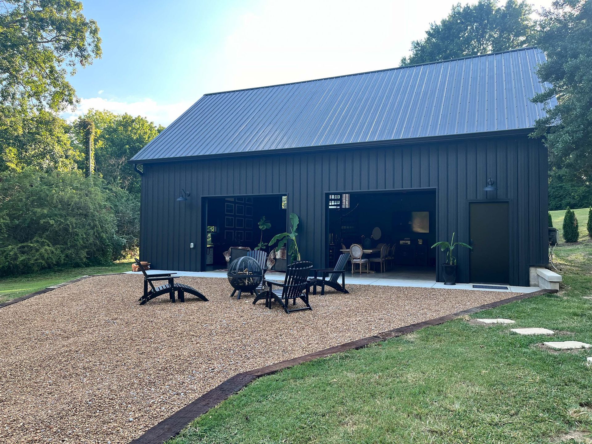 A large black barn with a fire pit in front of it.