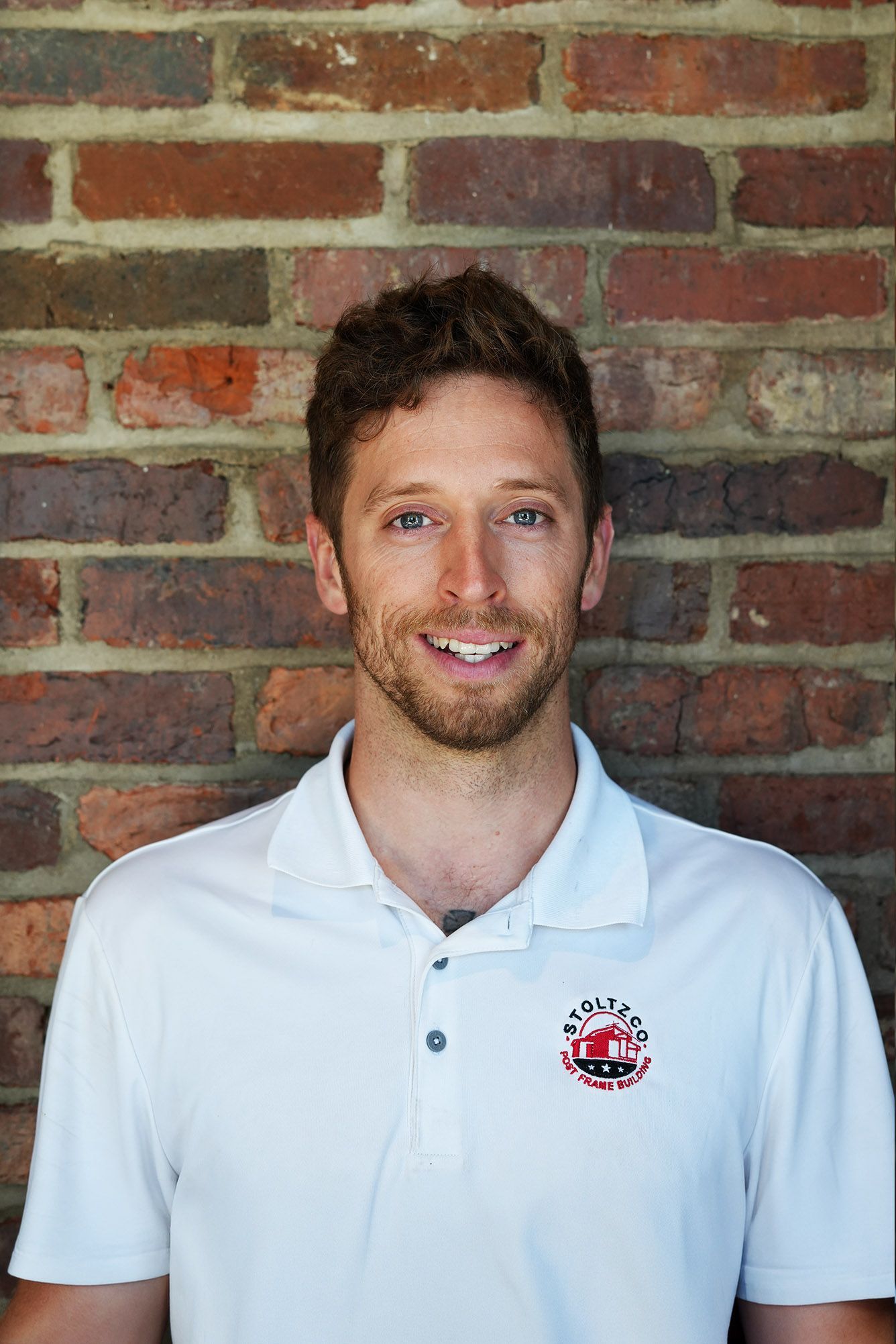 A man in a white shirt is smiling in front of a wooden wall